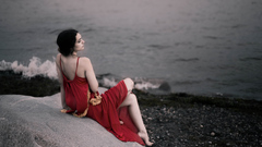 Girl In Red Dress Sitting On Rocks Beach